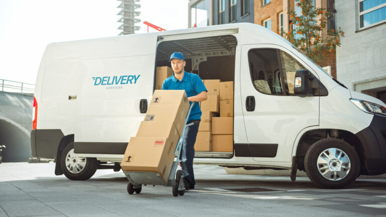 delivery man pushes hand truck trolley full of cardboard boxes.