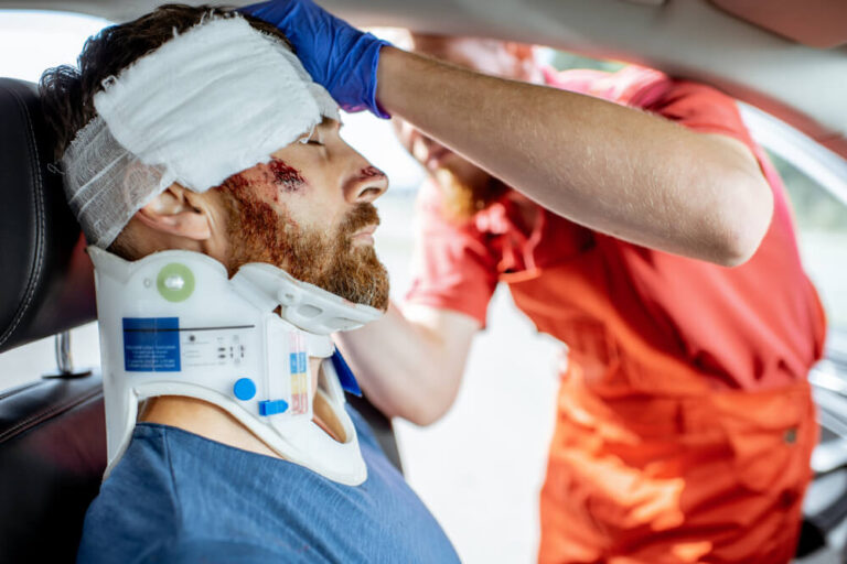 Medic applying bandage on the head of victim with serious damages sitting on the driver seat after the road accident.