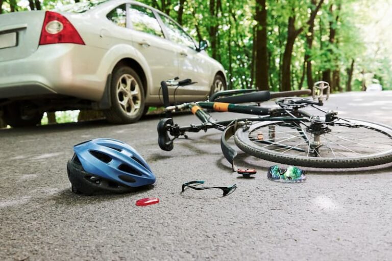 Bicycle and helmet on ground next to car, indicating accident.